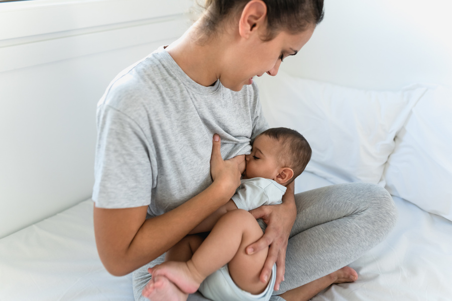 Happy mother breastfeeding her little baby on bed - Family and Maternity concept